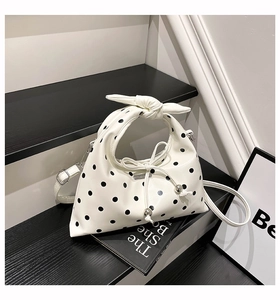 Close-up detail of white polka dot dumpling bag with side drawstring bow and knot handle
