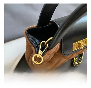 Detail of golden metal hooks and leather-woven chain strap on a quilted suede handbag