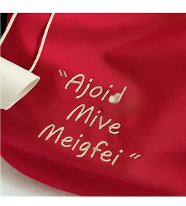 Detail of red canvas tote bag showing fine diagonal weave and beige letter embroidery