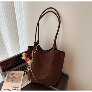 Detail of coffee brown suede tote bag with a small dog plush charm and slim shoulder straps