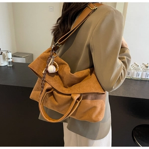 Detail of caramel suede tote bag with wide strap and creative baseball charm on model