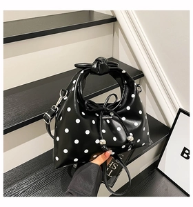 Close-up of black leather bag with white polka dots featuring knotted handle and bow detail