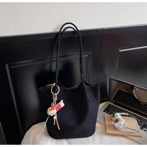 Detail of black tote bag with cute puppy charm and laptop on a minimalist white bed