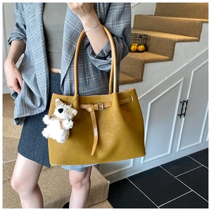 Gros plan d'un sac cabas jaune en similicuir tressé avec un petit ours en peluche
