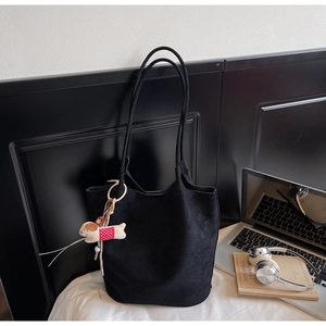 Detail of black suede tote bag with cute dog charm, laptop and headphone lifestyle setting