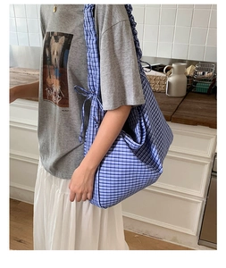 Detail view of a blue plaid tote bag with ruffled strap and side bow decoration