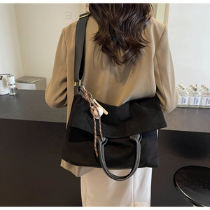 Close-up of black canvas tote bag with leather handles and decorative baseball pendant
