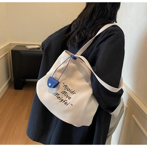 Detail of canvas tote bag showing side blue drawstring and minimalist letter print