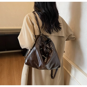 Detail view of large dark brown retro tote bag in glossy leather worn with beige trench coat