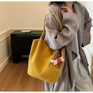Detail of yellow suede tote bag with white puppy plush pendant on model in trench coat