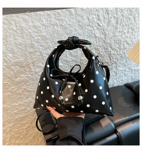 Detail of black polka dot dumpling bag with knotted handle and beaded bow on a leather bench