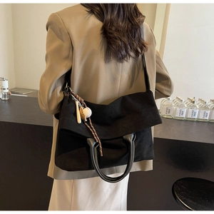 Close-up of black suede tote bag with cylinder handles and baseball charm accessory
