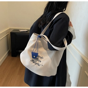 Detail of off-white canvas tote bag with black lettering and blue leather charm detail