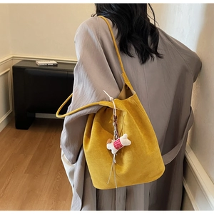 Macro shot of large yellow suede shoulder bag with a cute white dog plush pendant detail