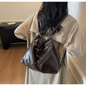Rear view of a model wearing a deep brown glossy leather backpack with thin straps