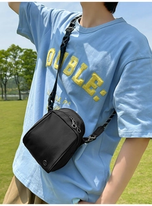 Detalle de correa ajustable y logo metálico redondo en bolso de nailon negro
