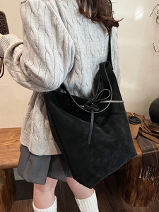 Black suede hobo bag with bow detail shown on shoulder in autumn lifestyle setting