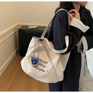 Close-up of cream canvas tote bag featuring black lettering and blue leather charm