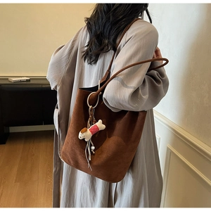 Detail of a large brown suede tote bag with cute dog charm worn on the shoulder
