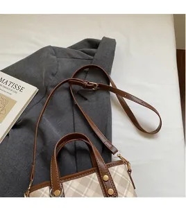 Close-up of khaki plaid bucket bag with adjustable leather strap and rivet details