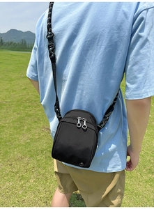 Foto al aire libre de un bolso bandolera de nailon negro con doble cremallera y correa