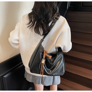 Detalle de un bolso hobo grande de cuero negro brillante con colgante decorativo marrón