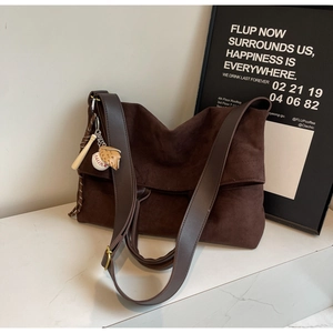 Detail of dark brown suede tote bag with leather strap and baseball charm on marble