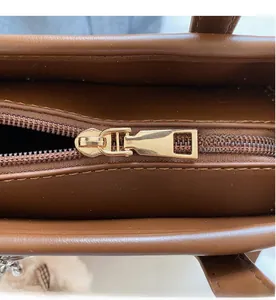 Detailed macro view of smooth golden metal zipper and brown leather texture on handbag