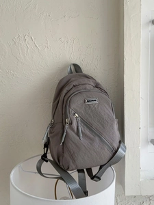 Minimalist taupe nylon backpack with MACHUGE logo patch and multiple zipper pockets