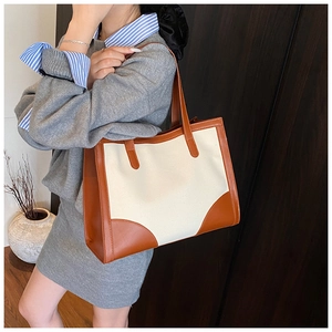Détail d'un grand sac fourre-tout en toile et cuir marron porté par un mannequin en extérieur