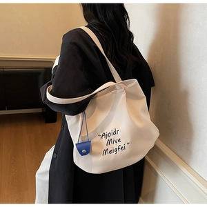 Detailed view of cream canvas tote bag with letter print and blue mini pouch accessory