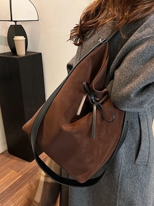 Brown suede tote bag with black strap shown on model in a warm minimalist studio