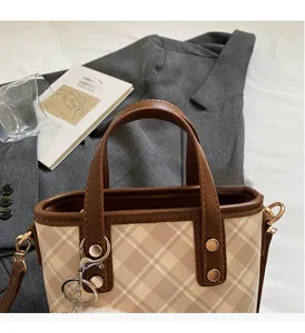 Detail of plaid canvas handbag with leather trim, metal rivets and fluffy pompom charm