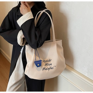 Detail of oatmeal canvas tote bag featuring black lettering and a blue mini charm pendant