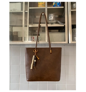 Close-up of vintage dark brown oil wax tote bag featuring ethnic beaded tassel detail