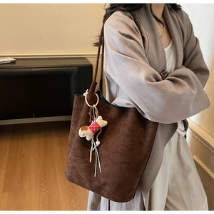 Detail of a large brown suede tote bag featuring a cute white puppy plush charm on the strap