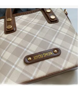 Detailed view of checkered handbag with brown leather trim and golden metal rivet accents