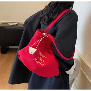 Detail of red canvas tote bag with white embroidery and shoulder strap on a model