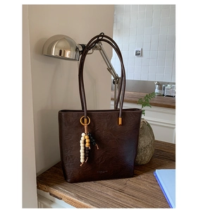 Detail of dark brown vintage tote bag with wooden bead tassel charm on wooden desk