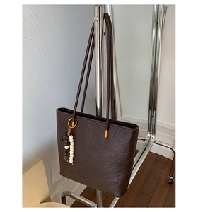 Detail of dark brown tote bag featuring slender straps and a three-color beaded keychain