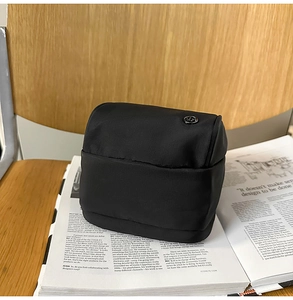 Detalle del bolso bandolera pequeño de nailon negro con logo metálico sobre revista