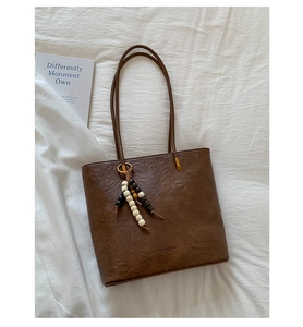 Detailed view of coffee brown leather tote bag with vintage texture and beaded keychain accessory