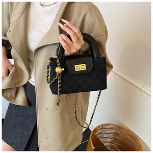 Detail of black quilted crossbody bag with golden turn-lock and ball chain strap