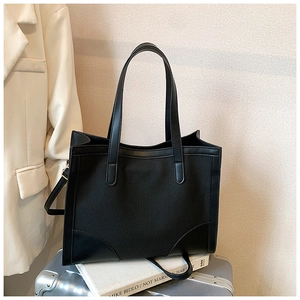 Détail du sac cabas en toile noire avec garniture en cuir sur une valise argentée