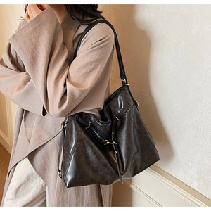 Detail of black matte leather tote bag with gold buckle and adjustable drawstring on model