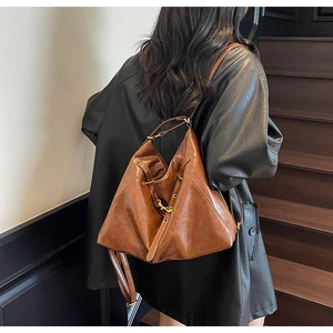 Rear view of a caramel brown leather hobo bag worn by a model on a shoulder