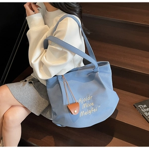 Close-up of blue canvas tote bag with yellow embroidery and leather coin purse charm