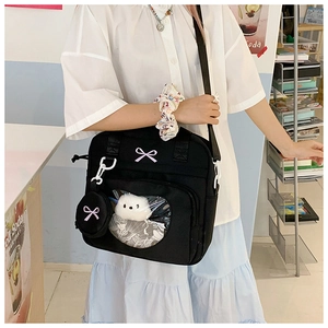 Detail of black canvas ita bag featuring a clear window with plush doll and bow embroidery
