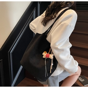 Detail of a large black suede tote bag featuring a cute plush dog charm on a wooden staircase