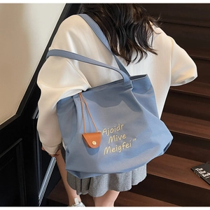 Detail of blue canvas tote bag with letter embroidery and brown mini leather pouch charm